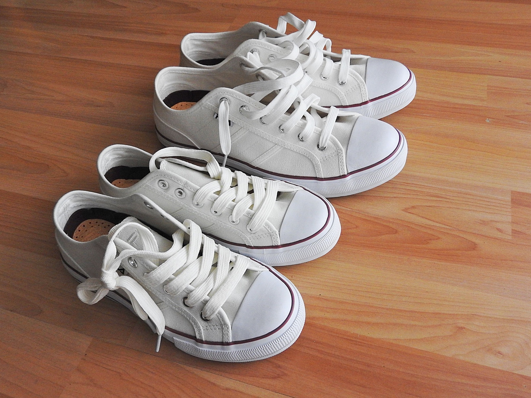 Four white sneakers arranged on an empty wooden floor